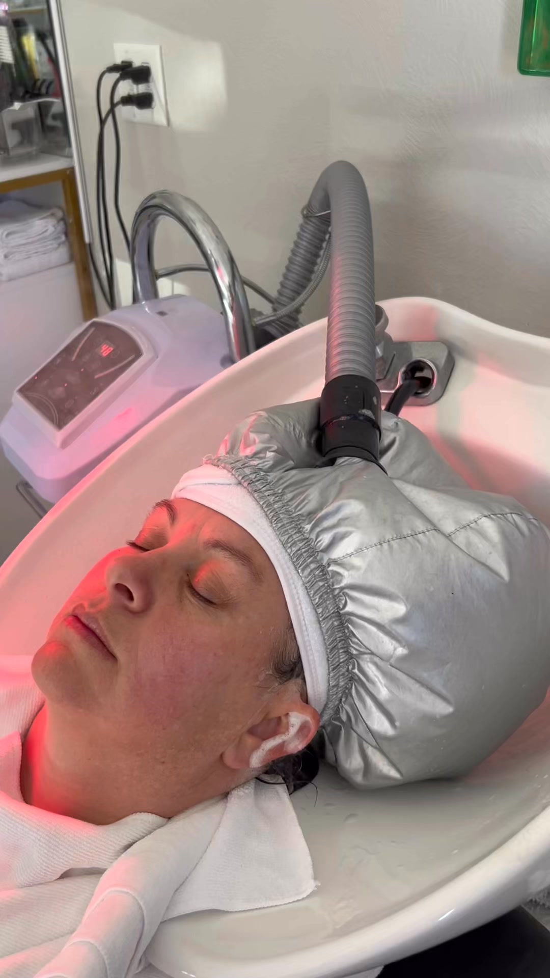 A client relaxing under warm red light therapy during a Scalp Facial at Studio M salon